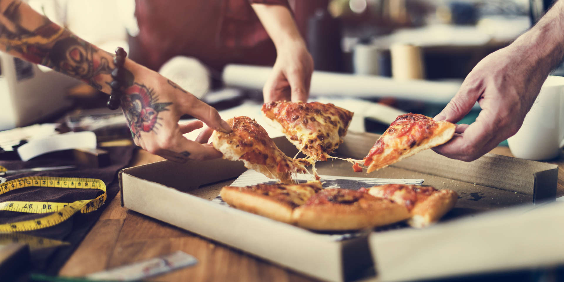 Pizza im Karton, mehrere Personen greifen sich ein Stück Pizza
